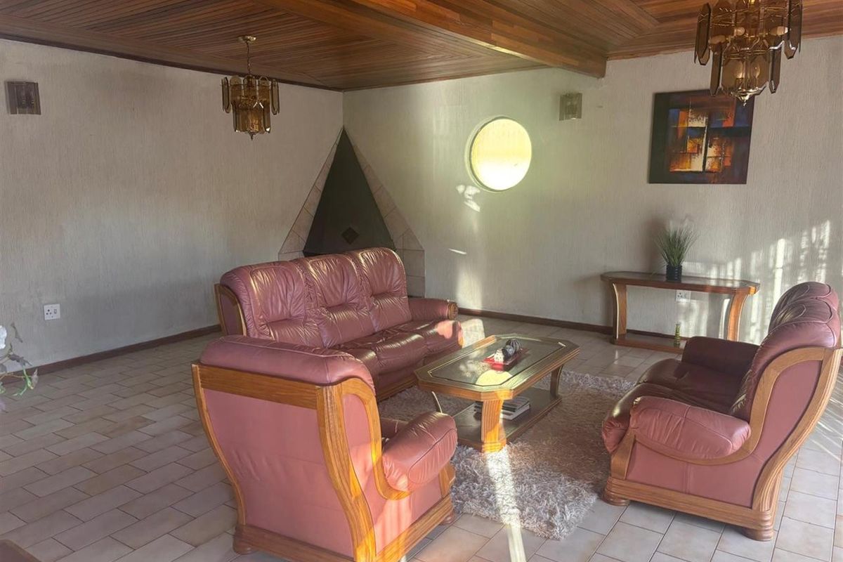 Spacious living room featuring a unique triangular corner fireplace, circular accent window, and distinctive wood-paneled ceiling.