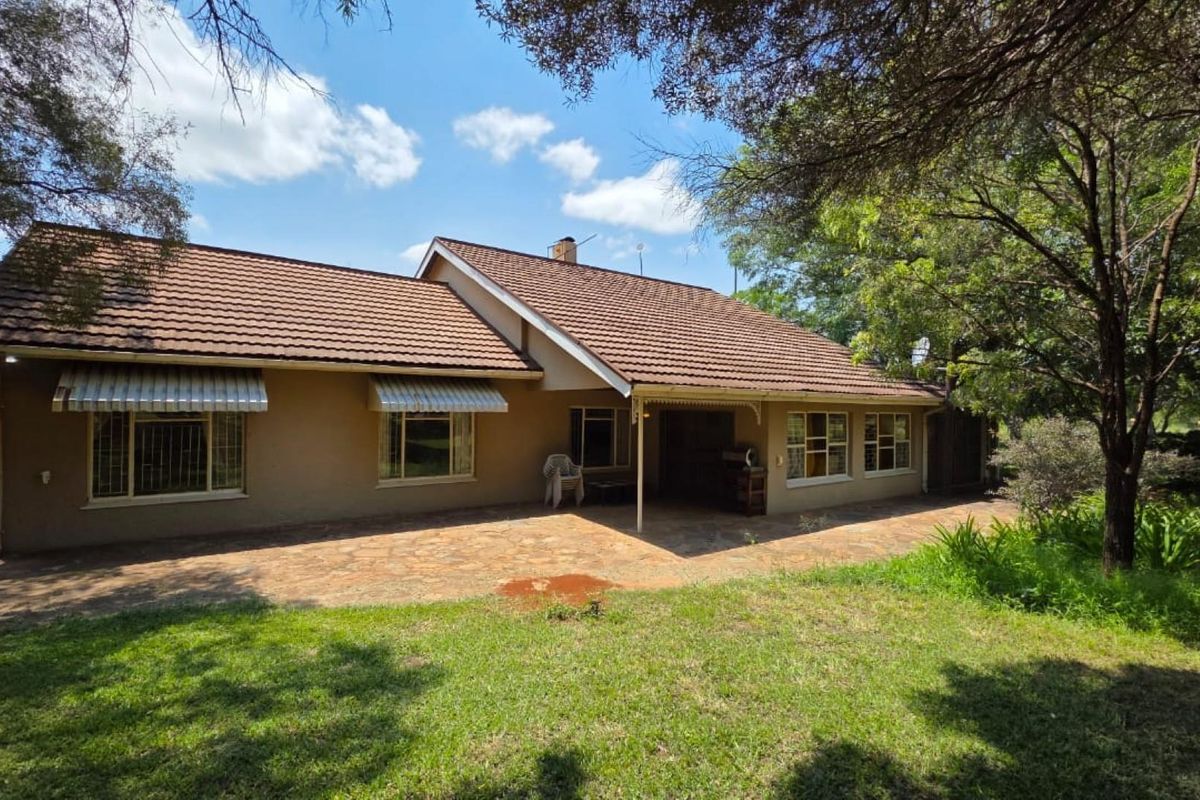 Rear view of a farm-style residence featuring a tiled roof, covered patio area, and established garden surroundings.