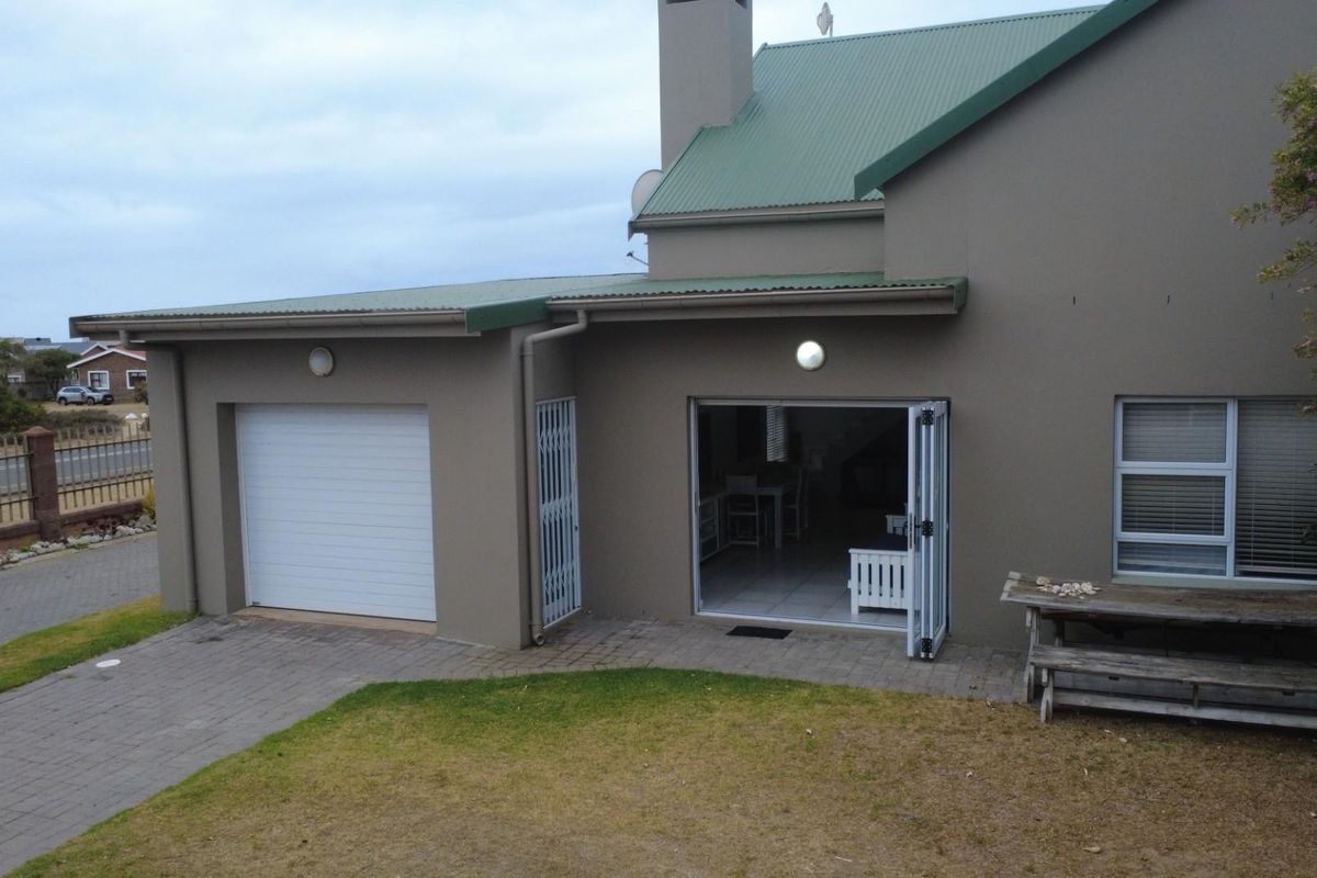 Rear view of the townhouse featuring a single garage, paved patio area, and folding glass doors leading into the interior living space.