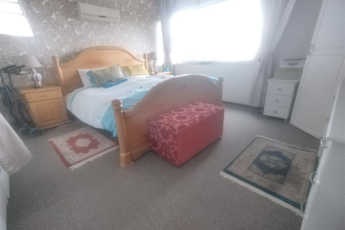 A bedroom featuring a split-system air conditioner and built-in wardrobe storage, with carpeted flooring and a large window providing natural light.