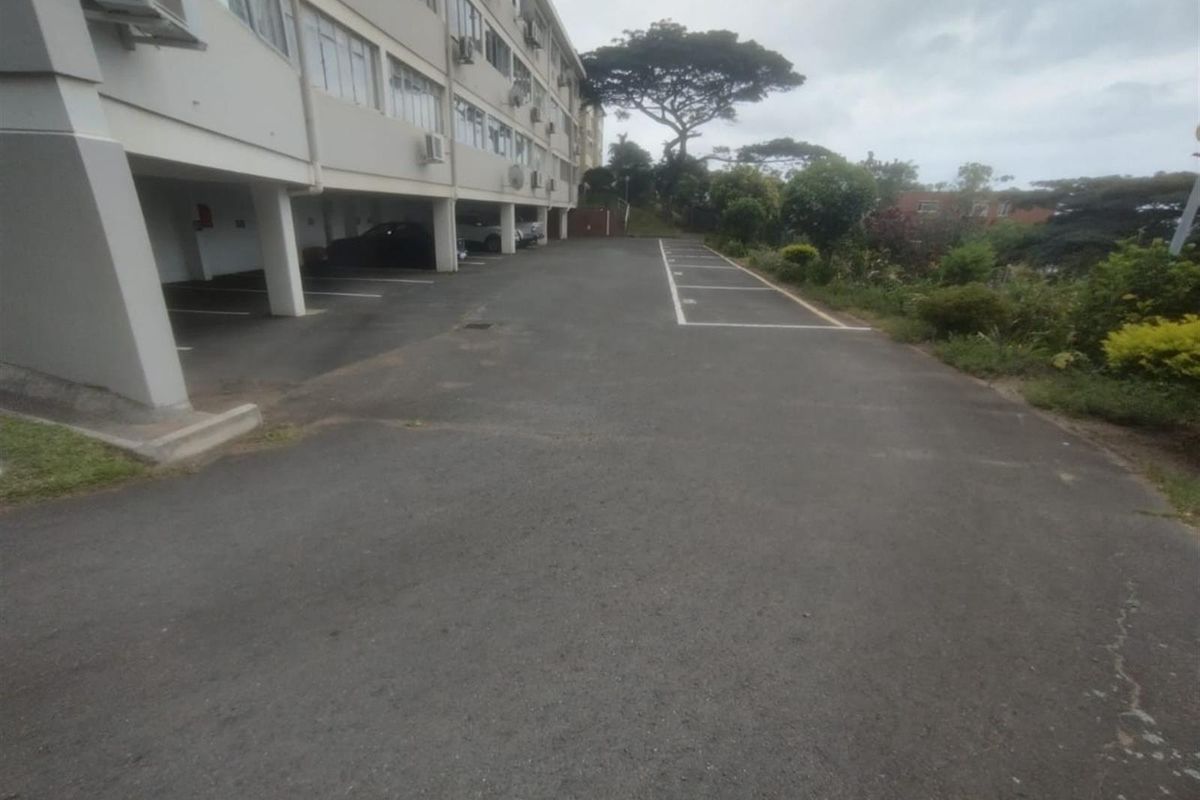 Exterior view of the apartment complex showing the rear parking area with covered bays and paved driveway.