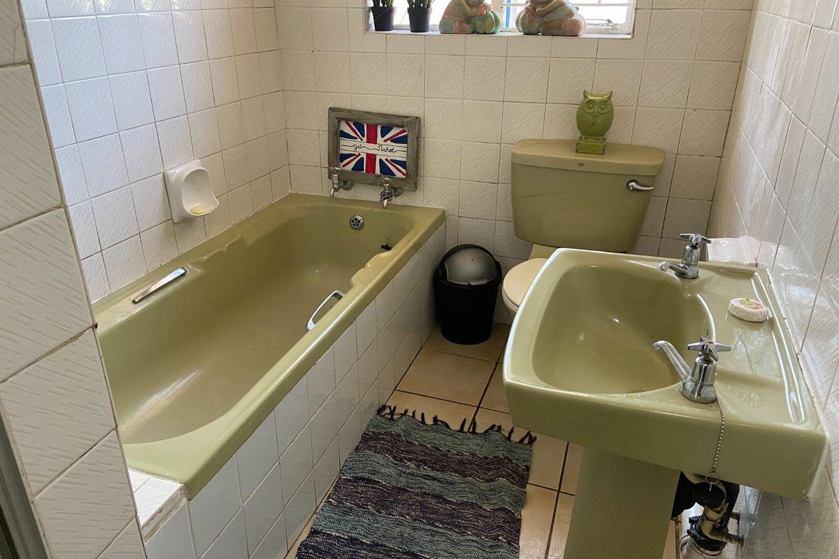 A dated bathroom featuring original avocado green sanitaryware, including a bathtub and pedestal basin, with white wall tiling and tiled flooring.
