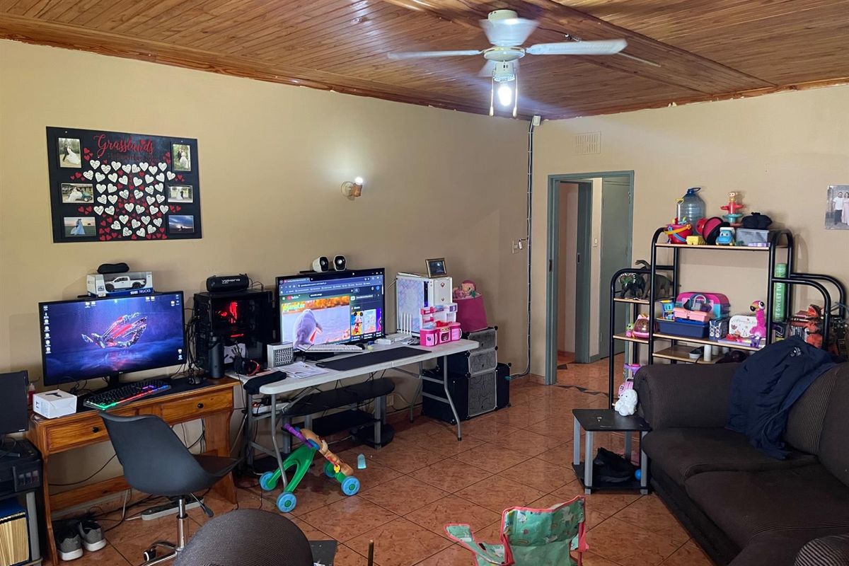 A living room featuring a timber-clad ceiling, ceiling fan, and tiled flooring, currently utilized as a multi-purpose living and workspace area.