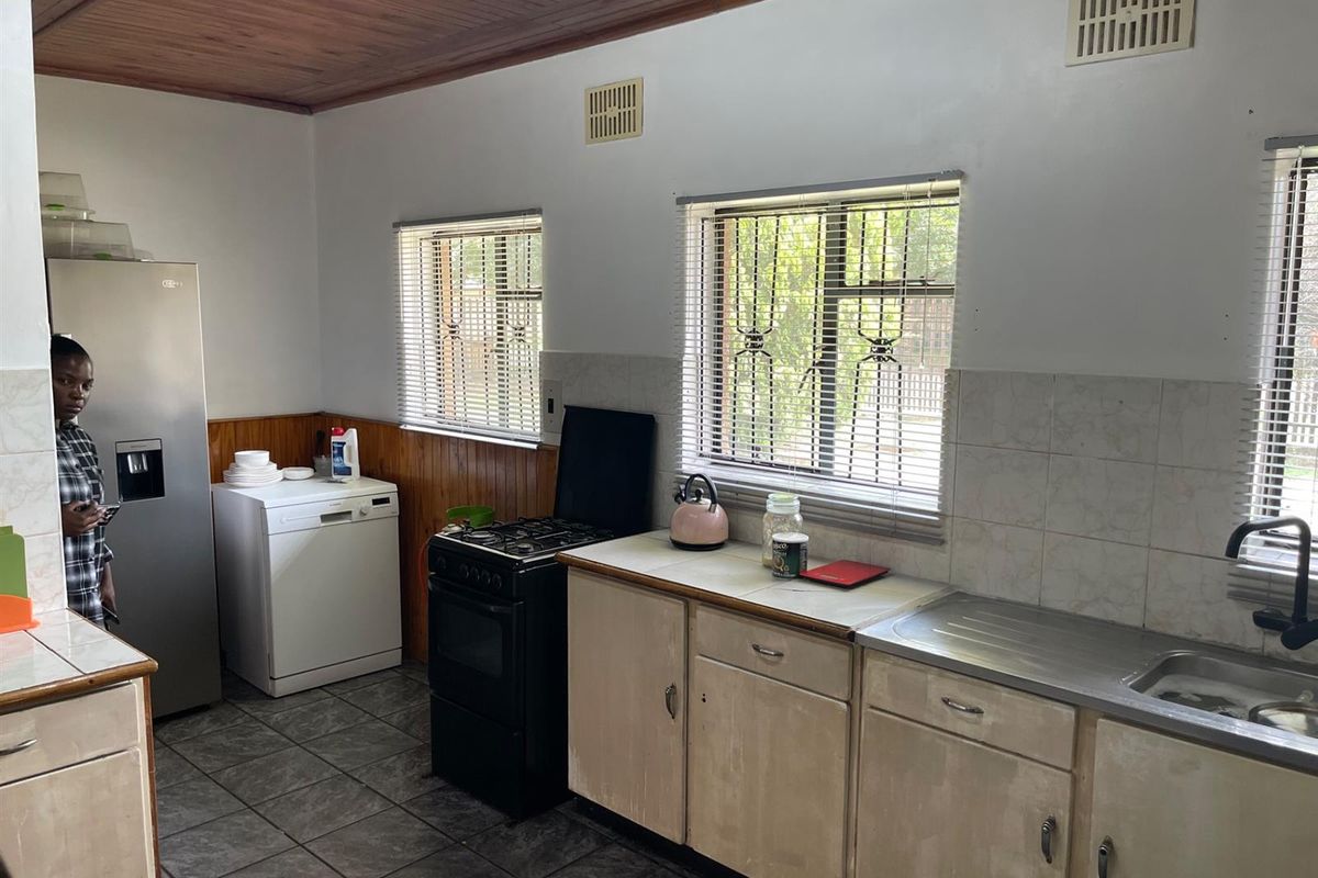 A functional kitchen featuring tiled flooring, built-in cabinetry, a stainless steel sink, and a freestanding stove, with timber ceiling accents.