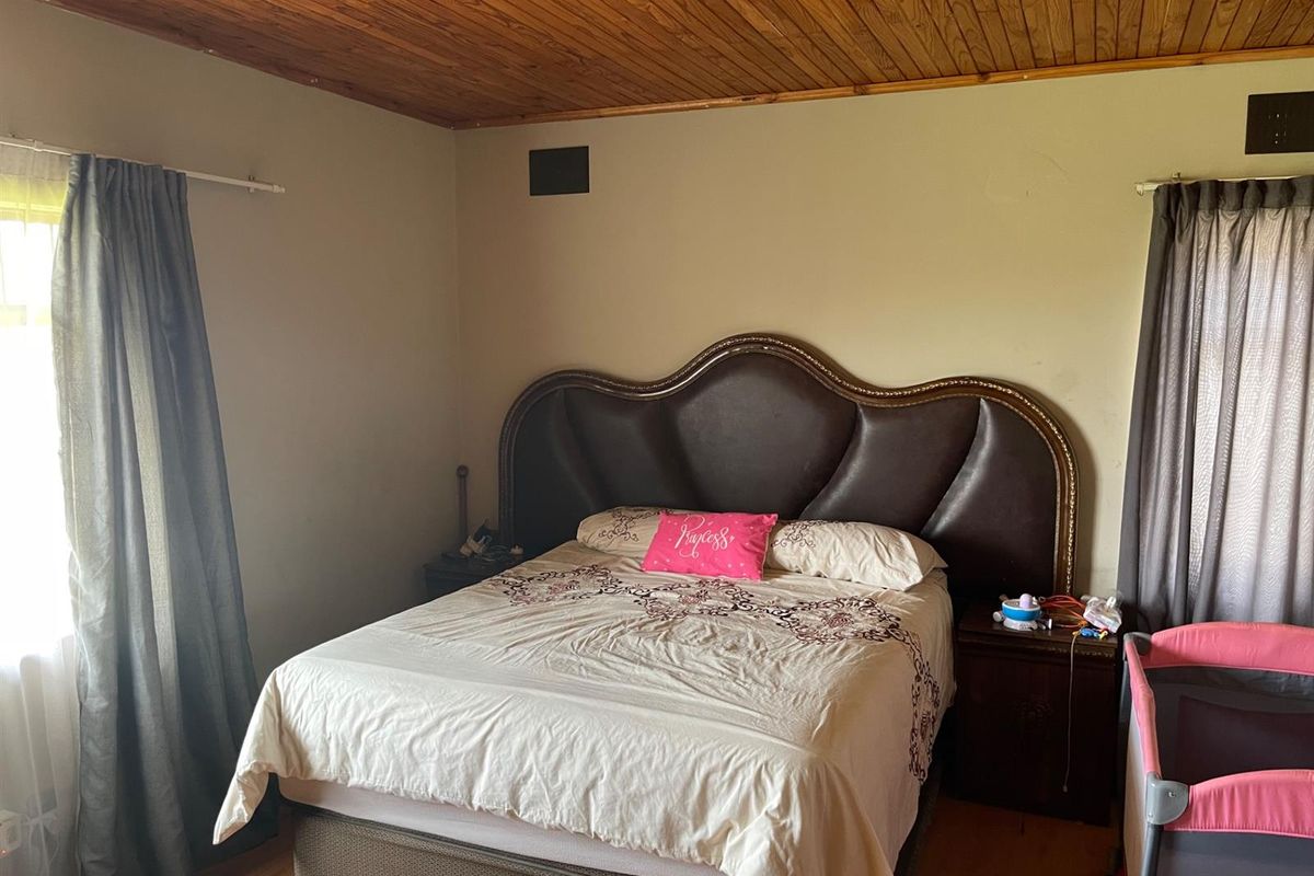 A bedroom featuring a timber-paneled ceiling and laminate flooring, providing a functional space with natural light from the side window.