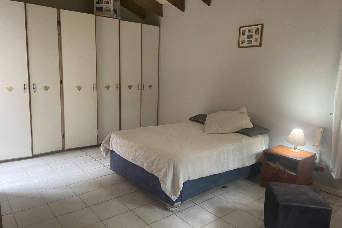 A bedroom featuring exposed timber ceiling beams, tiled flooring, and extensive built-in wardrobe storage.