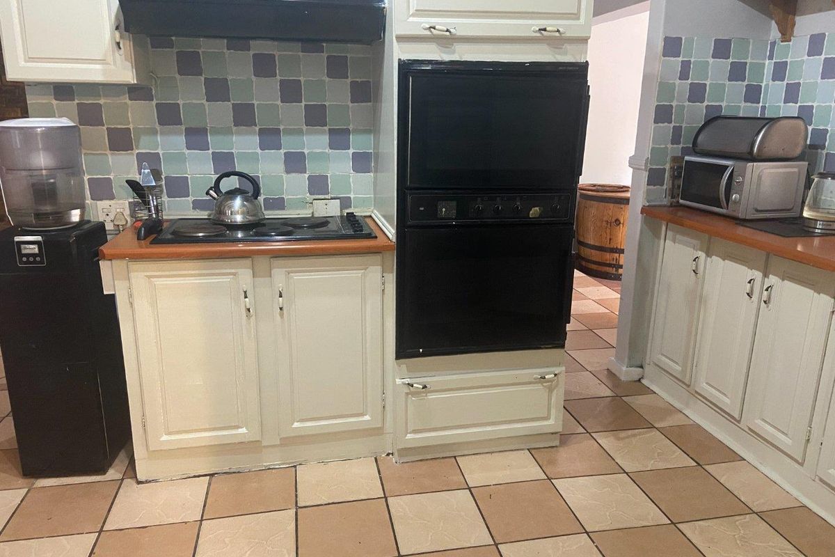 A dated kitchen featuring built-in cabinetry, a wall-mounted oven, a hob with an extractor fan, and tiled flooring.