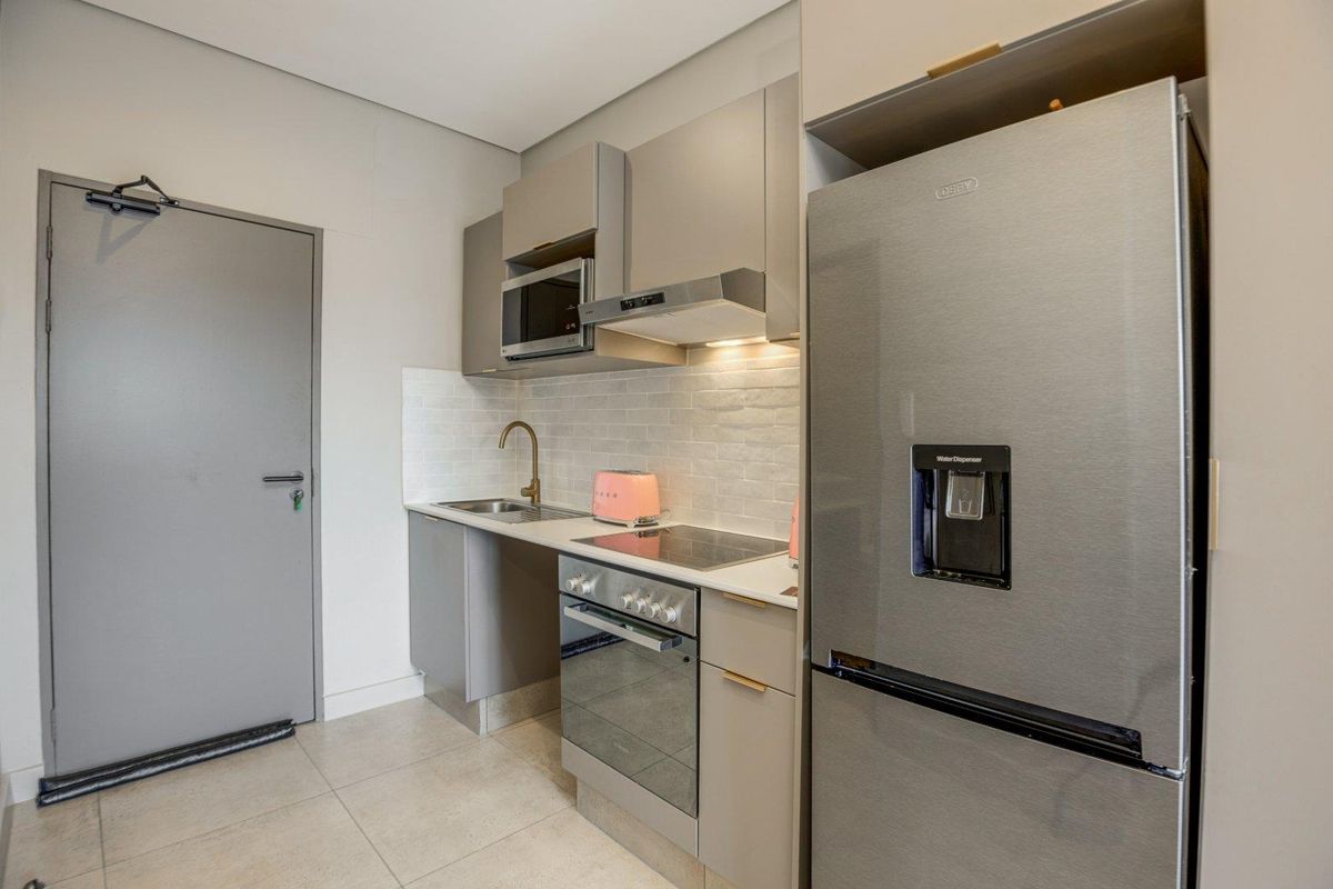 Modern compact kitchen featuring sleek grey cabinetry, integrated appliances including an oven and hob, tiled backsplash, and neutral floor tiles.