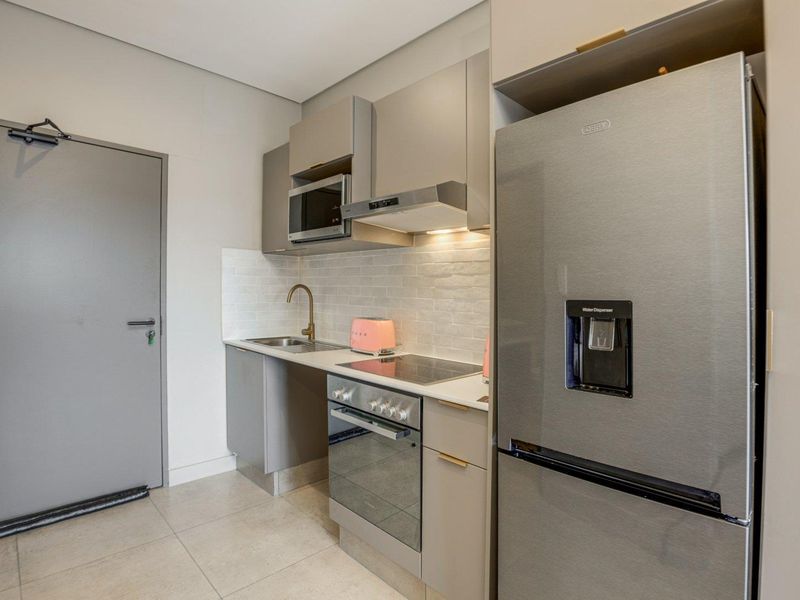Modern compact kitchen featuring sleek grey cabinetry, integrated appliances including an oven and hob, tiled backsplash, and neutral floor tiles.