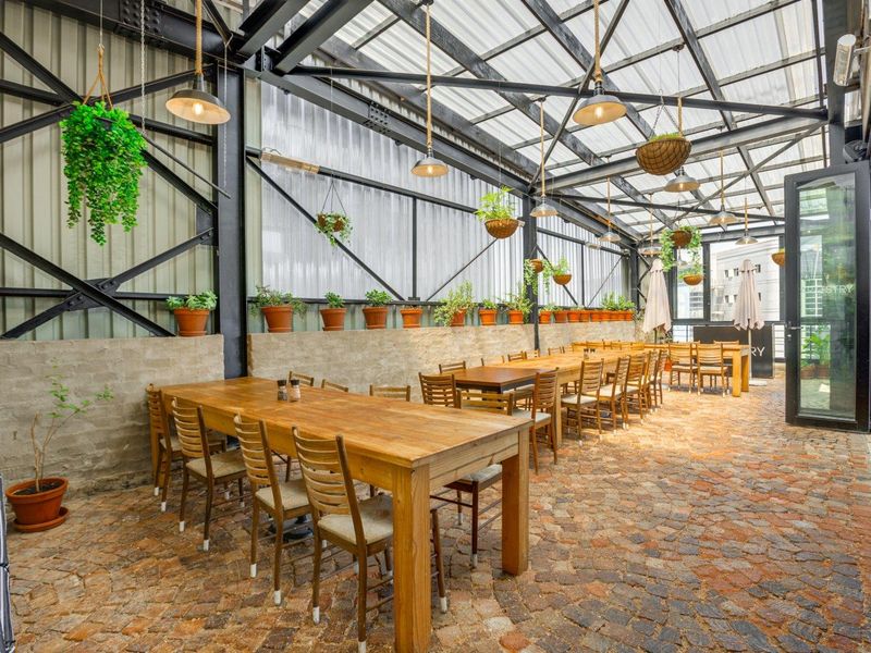 A spacious covered outdoor patio featuring exposed steel structural beams, a translucent roof, and durable cobblestone flooring, ideal for dining and entertainment.