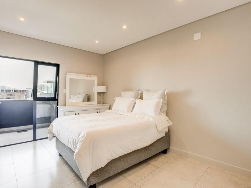 A well-maintained bedroom featuring neutral walls, tiled flooring, recessed lighting, and direct access to a private balcony through a sliding glass door.
