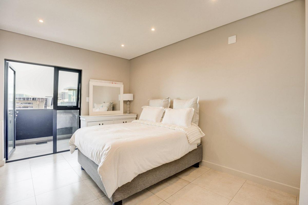 A well-maintained bedroom featuring neutral walls, tiled flooring, recessed lighting, and direct access to a private balcony through a sliding glass door.
