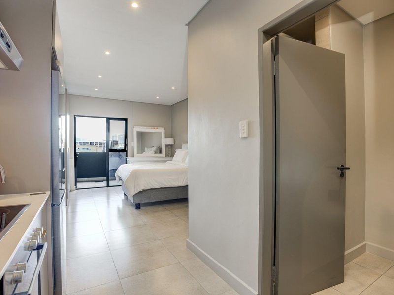 Modern open-plan apartment layout featuring a compact kitchen area flowing into a bedroom space with access to a private balcony.