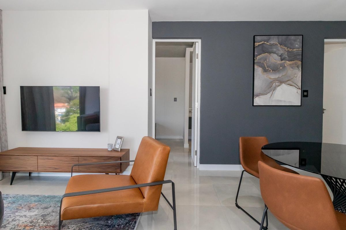 A modern, well-maintained living area featuring neutral tiled flooring, a contrasting dark accent wall, and seamless access to the adjacent hallway.