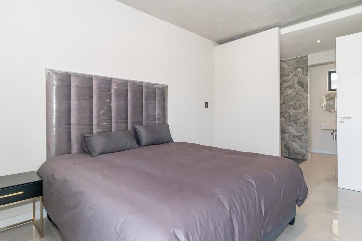 Modern bedroom featuring neutral tones, tiled flooring, and direct access to an en-suite bathroom with marble-style wall finishes.