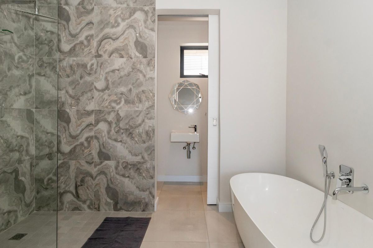 Modern bathroom featuring a sleek freestanding bathtub, a spacious walk-in shower with decorative feature tiling, and a minimalist wall-mounted basin.