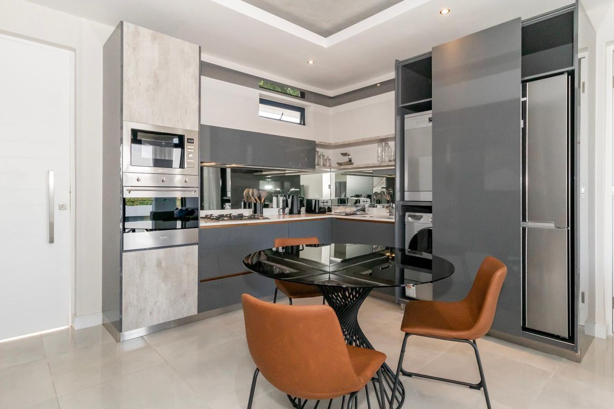 Modern kitchen featuring high-gloss cabinetry, integrated appliances, a mirrored splashback, and recessed ceiling lighting, offering a sleek and functional culinary space.