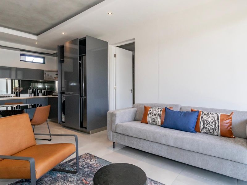 Modern open-plan living area featuring a sleek kitchen with built-in appliances, recessed ceiling lighting, and polished tiled flooring throughout.