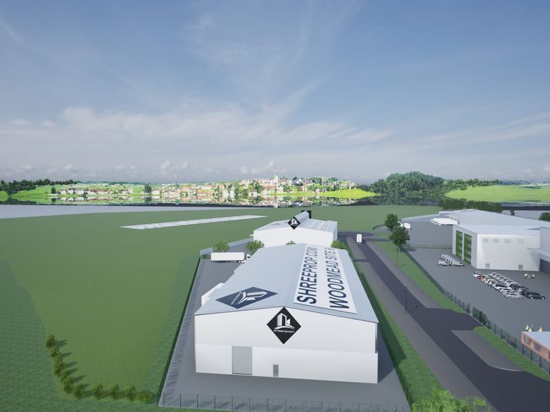 An aerial view of an industrial site featuring multiple warehouse buildings, paved access roads, and perimeter fencing in a landscaped setting.