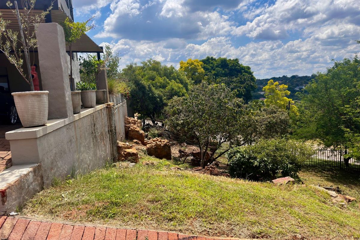 A view of the rear garden area featuring a retaining wall, established trees, and a brick-paved border overlooking the surrounding landscape.