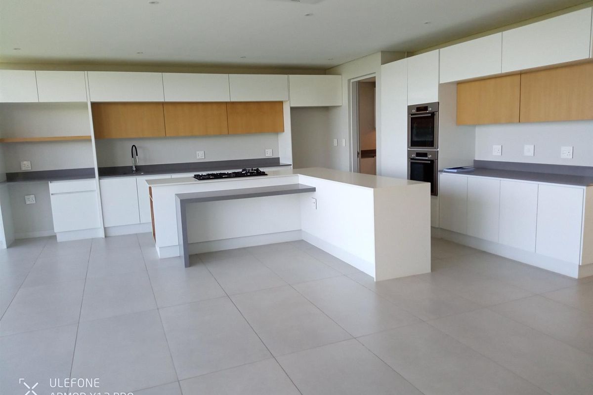 Modern, spacious kitchen featuring sleek white and wood-tone cabinetry, a central island with a gas hob, and integrated double wall ovens.