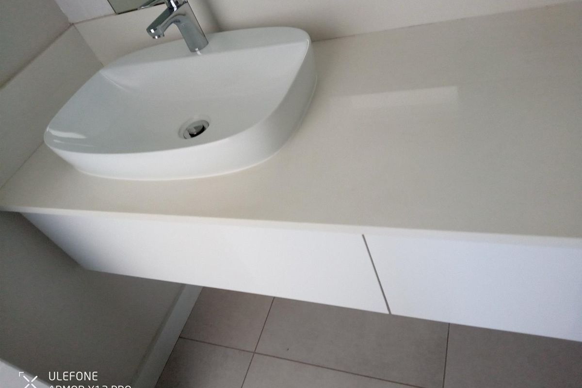 A modern, minimalist bathroom vanity featuring a sleek countertop basin, chrome mixer tap, and wall-mounted cabinetry with clean lines and neutral tiled flooring.