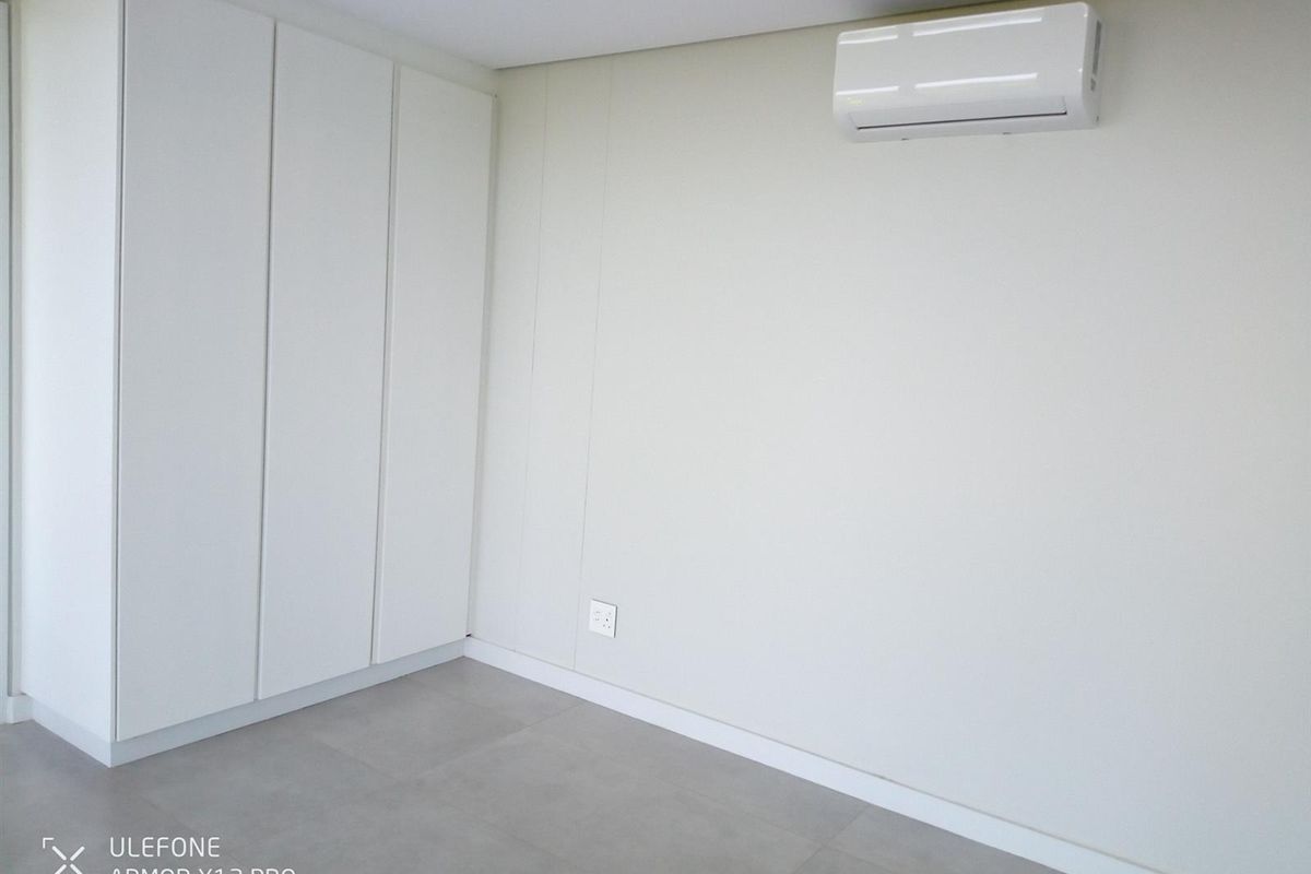 A clean, modern bedroom featuring neutral tiled flooring, ample built-in cupboard storage, and a wall-mounted split-system air conditioning unit.