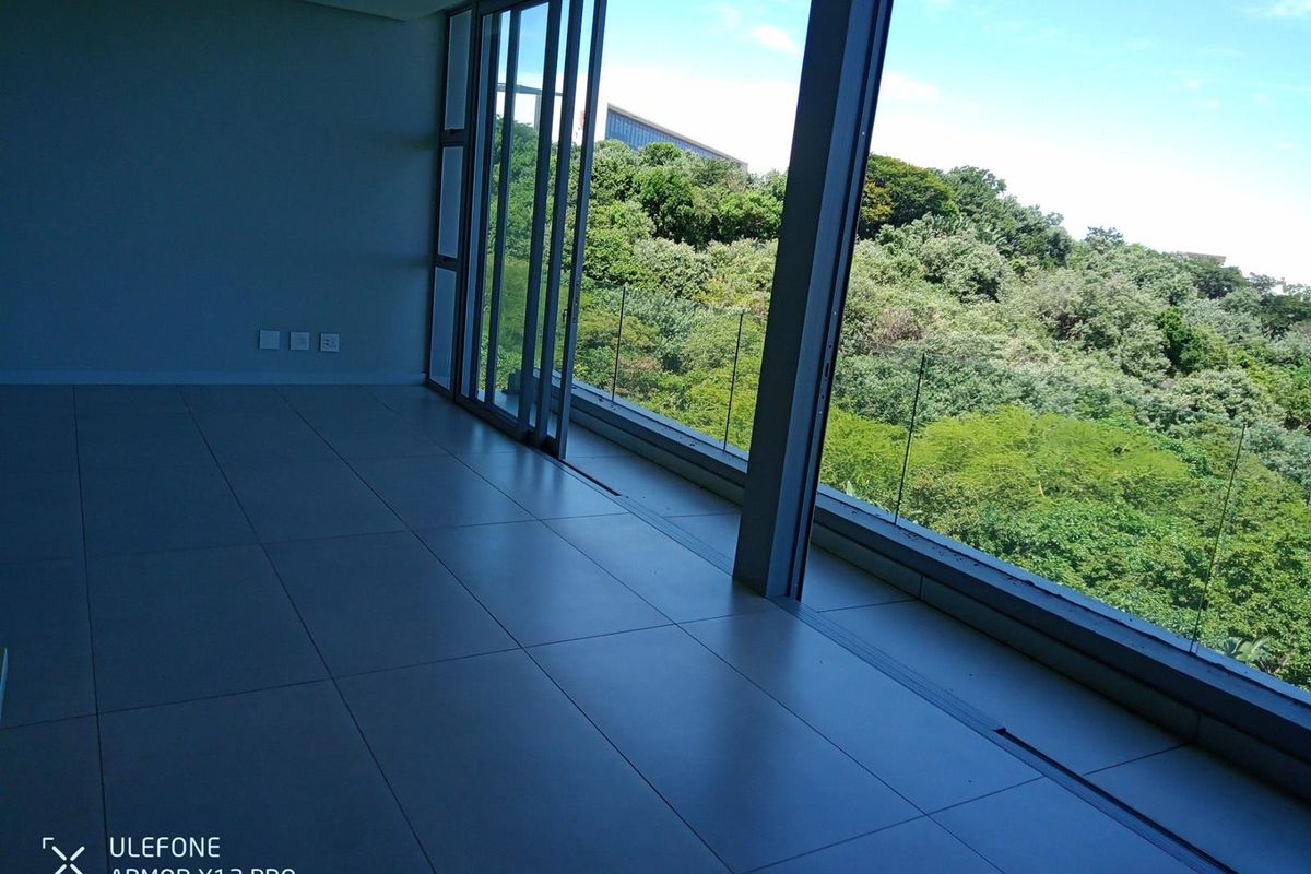 Spacious, empty living area featuring large format floor tiles and expansive sliding glass doors opening to a scenic, elevated green view.