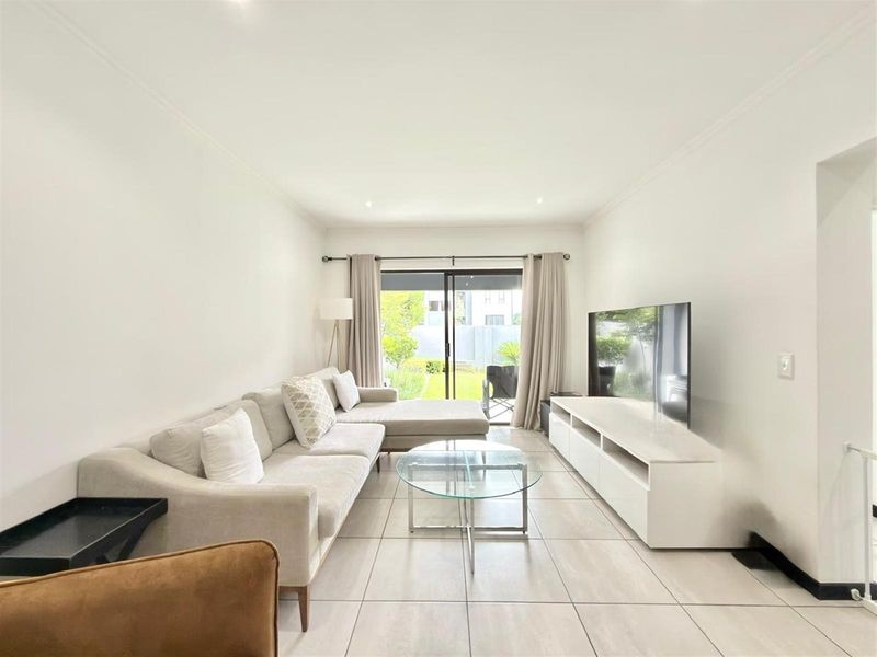 A bright and modern living room featuring large format floor tiles, recessed lighting, and a sliding glass door providing direct access to the outdoor area.