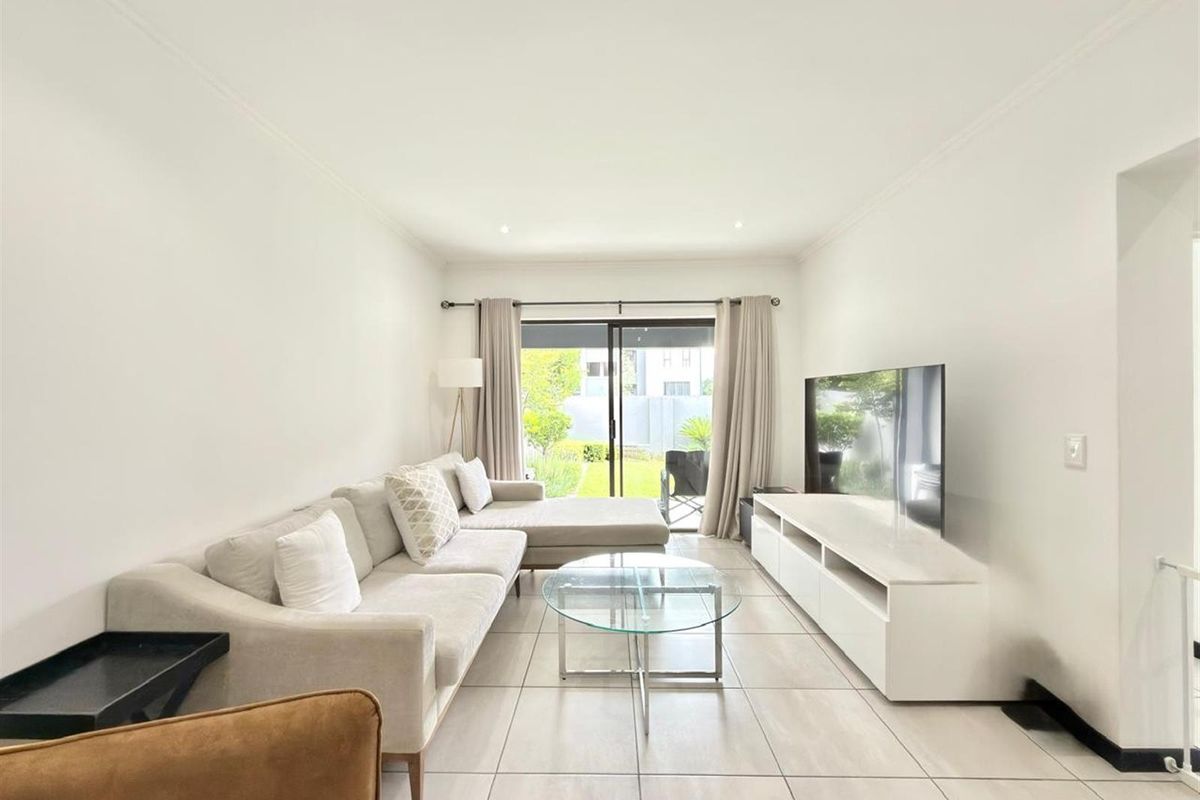A bright and modern living room featuring large format floor tiles, recessed lighting, and a sliding glass door providing direct access to the outdoor area.