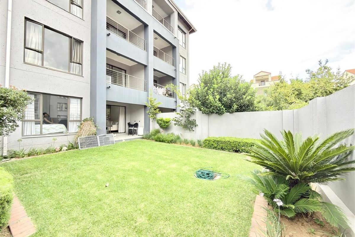 A well-maintained rear garden area featuring a manicured lawn, landscaped borders, and a boundary wall, adjacent to the apartment building's balconies.