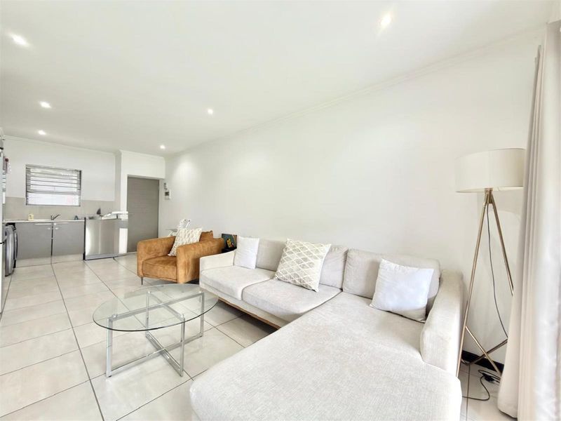 Open-plan living area featuring neutral tiled flooring, recessed downlighting, and a functional kitchen space with built-in cabinetry and stainless steel sink.