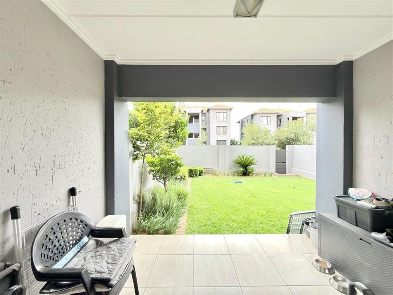 A covered patio area featuring tiled flooring and structural columns, overlooking a private garden space with a lawn and boundary wall.