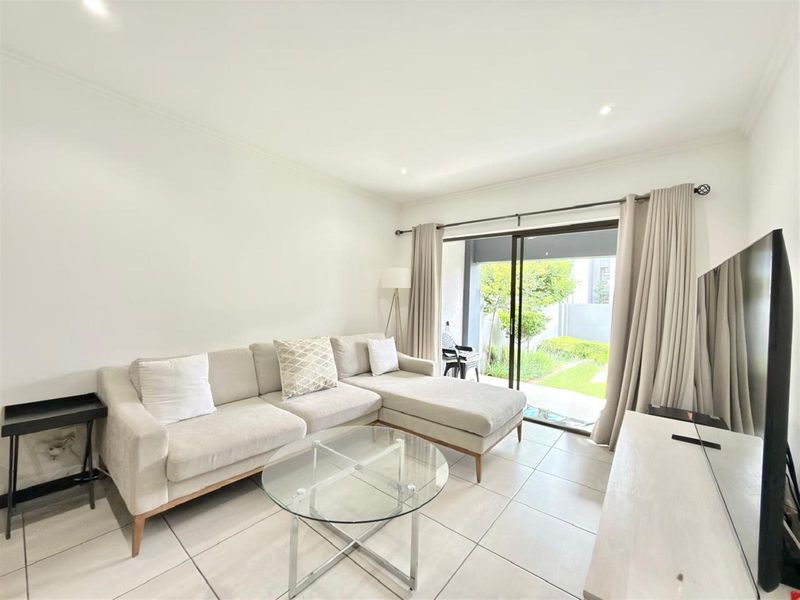A bright and modern living room featuring large format floor tiles and a sliding glass door providing direct access to the outdoor patio area.