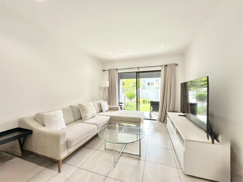 Bright and modern living room featuring neutral tiled flooring, recessed lighting, and a large sliding glass door providing direct access to the outdoor area.