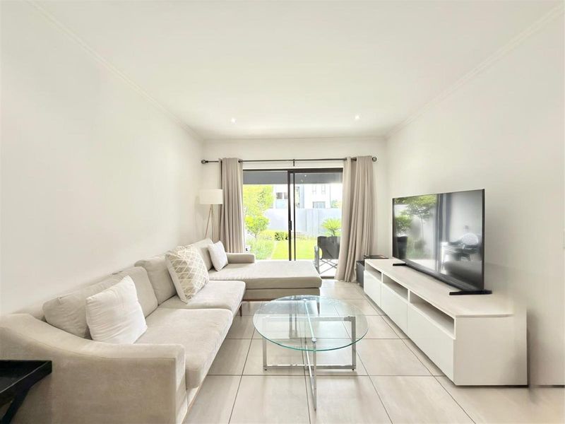 A bright and well-maintained living room featuring neutral tiled flooring, recessed lighting, and a large sliding glass door providing access to the garden.