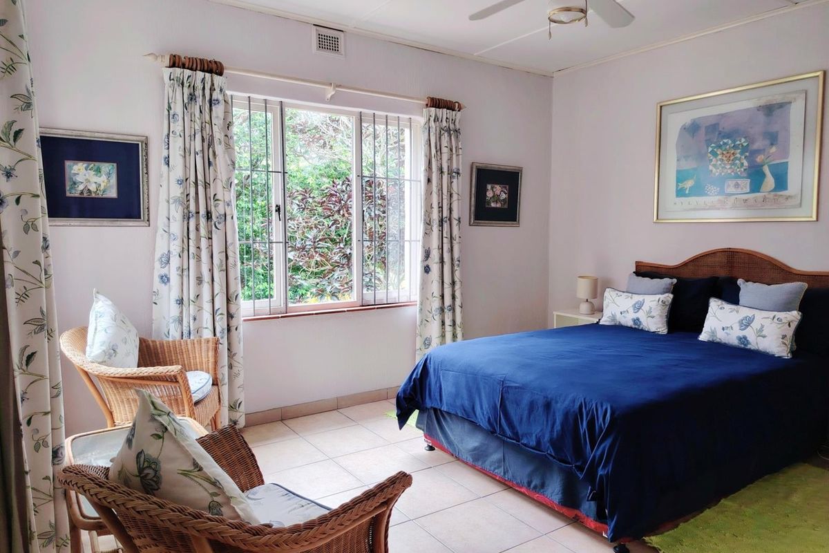 A well-lit bedroom featuring tiled flooring, a ceiling fan, and a window with security bars, offering a comfortable and functional living space.