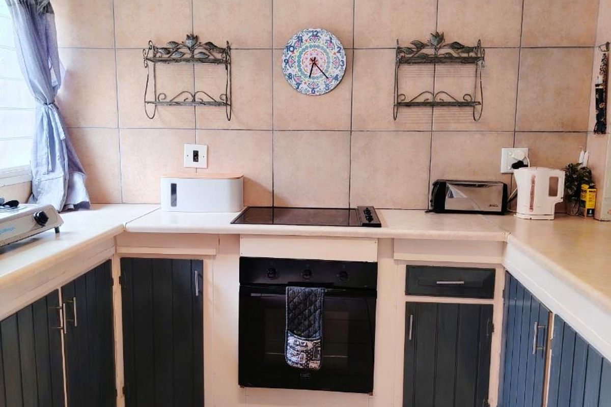 A functional kitchen featuring a built-in oven, electric hob, tiled splashback, and fitted cabinetry with tiled flooring.