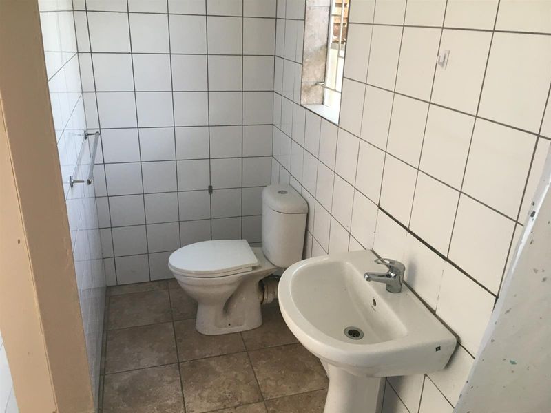 A compact bathroom featuring a pedestal basin, toilet, and white wall tiling. The space is functional but would benefit from cosmetic updates.