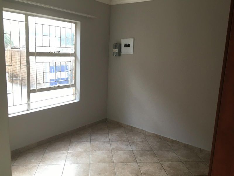 An empty bedroom featuring tiled flooring, security bars on the window, and a wall-mounted electrical distribution board and prepaid meter.