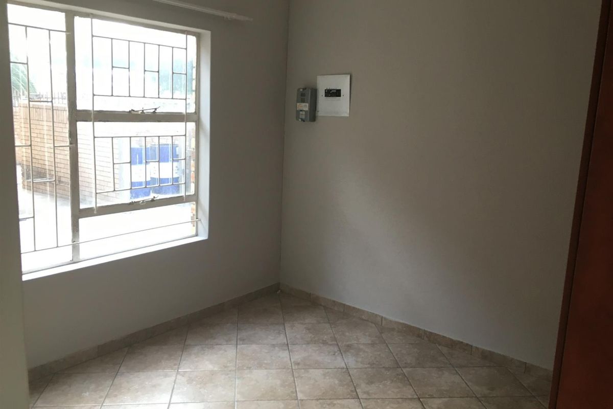 An empty bedroom featuring tiled flooring, security bars on the window, and a wall-mounted electrical distribution board and prepaid meter.