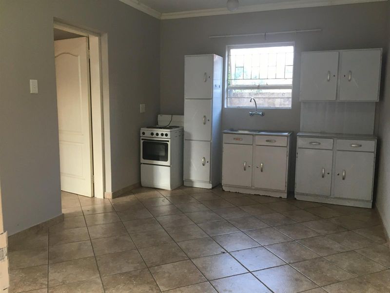 A functional kitchen featuring tiled flooring, built-in cabinetry, a stainless steel sink, and a freestanding stove, offering a blank canvas for potential updates.