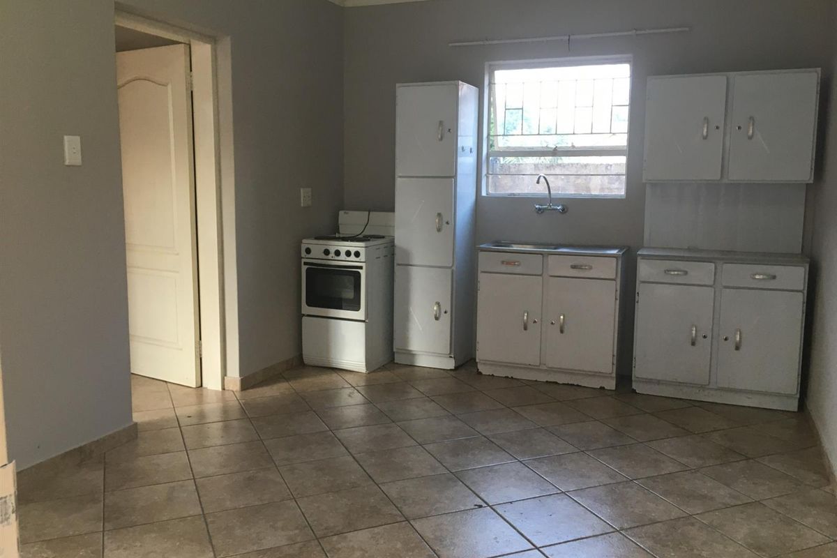 A functional kitchen featuring tiled flooring, built-in cabinetry, a stainless steel sink, and a freestanding stove, offering a blank canvas for potential updates.