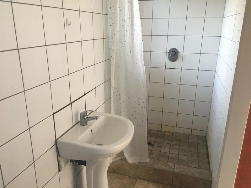 A functional bathroom featuring a pedestal washbasin and a tiled shower enclosure with a mixer tap.