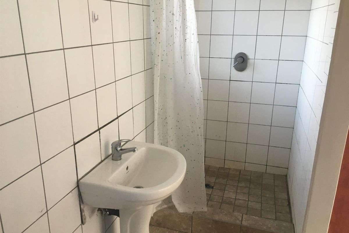 A functional bathroom featuring a pedestal washbasin and a tiled shower enclosure with a mixer tap.