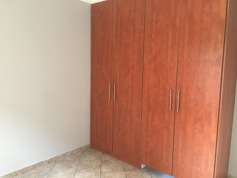 A clean, empty bedroom featuring neutral tiled flooring and ample built-in wooden cupboards for storage.