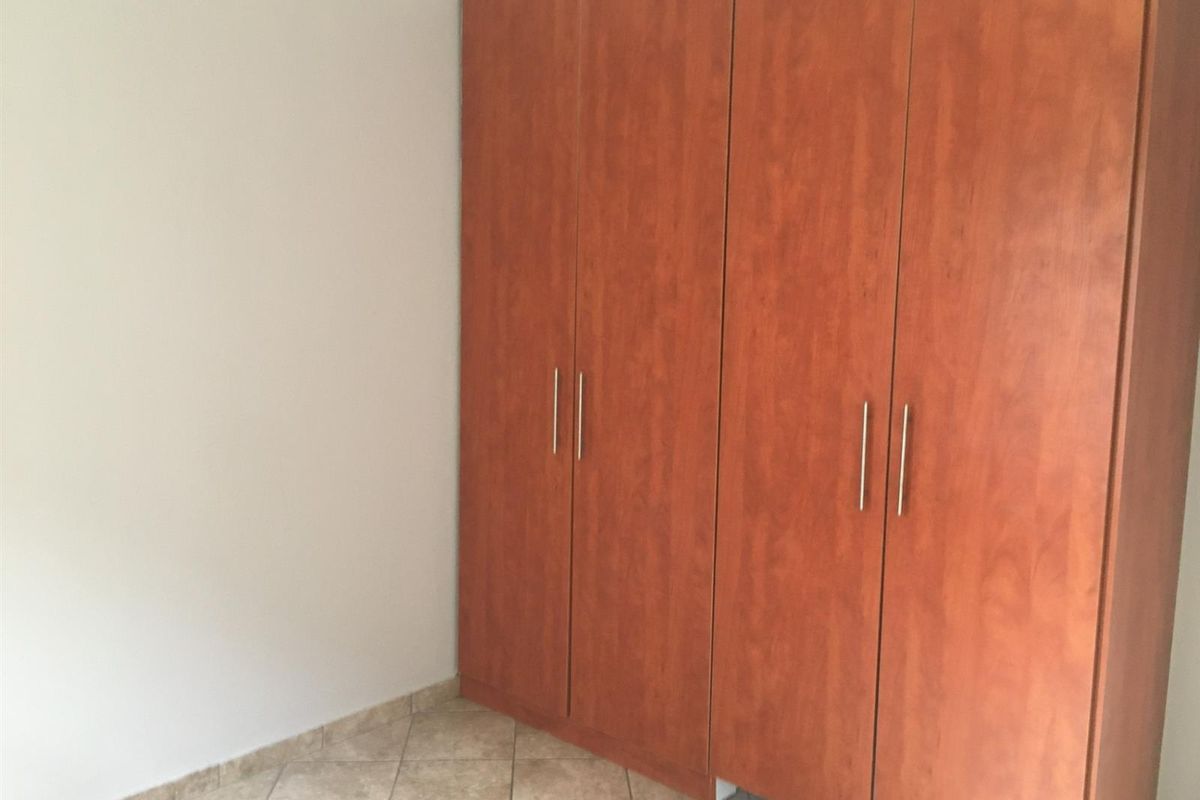 A clean, empty bedroom featuring neutral tiled flooring and ample built-in wooden cupboards for storage.