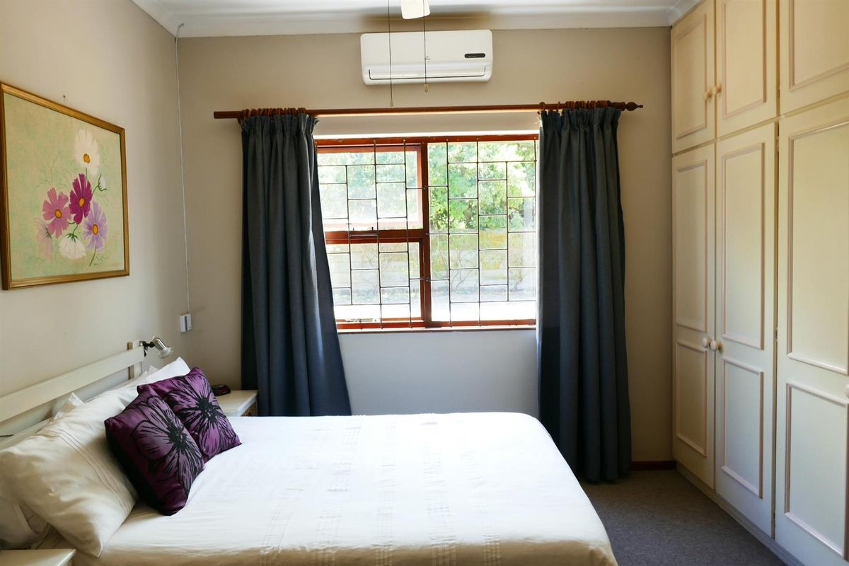 A bedroom featuring built-in cupboards, a wall-mounted air conditioning unit, and a window with security bars.