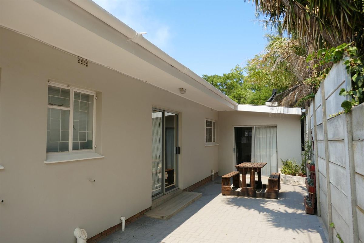 A paved rear patio area featuring sliding glass door access to the home, bordered by a concrete boundary wall and established garden greenery.