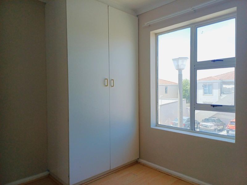 A bright bedroom featuring built-in white cabinetry and large windows providing natural light and a view of the surrounding complex.